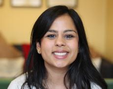 A photograph of Sheila Kanani smiling at the camera with a room blurred in the background